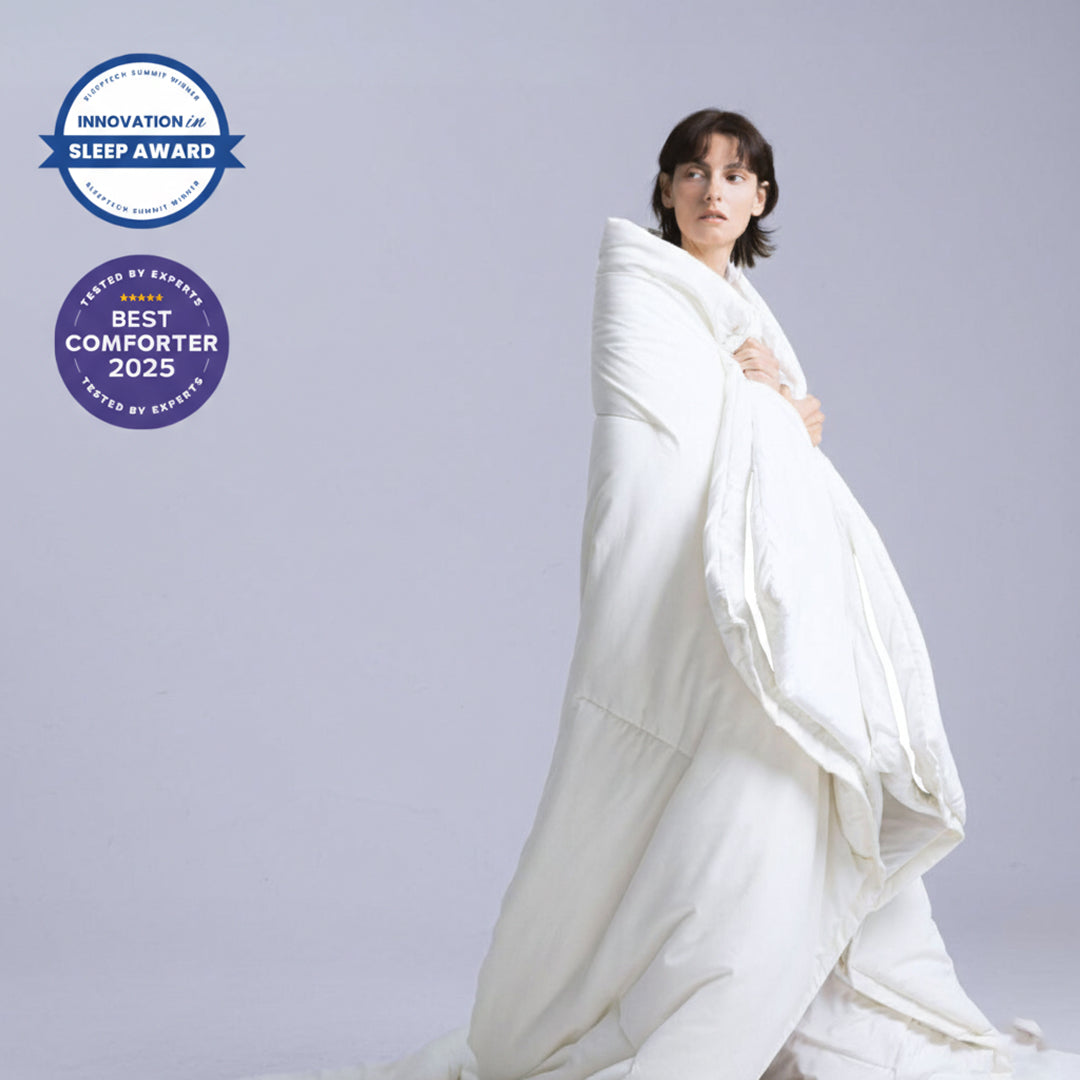 Person in pajamas under a purple and white blanket, smiling.